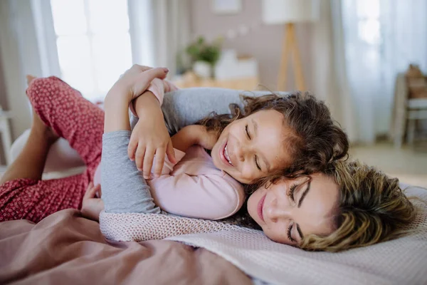 Щаслива мати лежить на ліжку зі своєю маленькою донькою і кокон вдома . — стокове фото