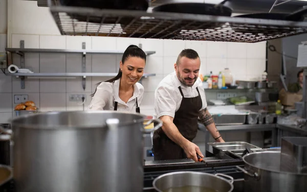 Happy chef and cook working on their dishes indoors in restaurant kitchen. — Stock Photo, Image