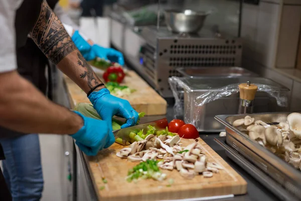 Cuoco irriconoscibile con guanti che tagliano verdure al chiuso in cucina ristorante. — Foto Stock