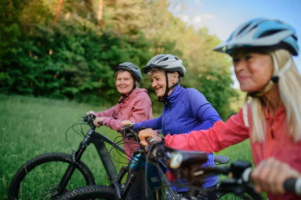 Feliz activo senior amigos mujeres empujando bicicletas juntos al aire libre en la naturaleza. — Foto de Stock