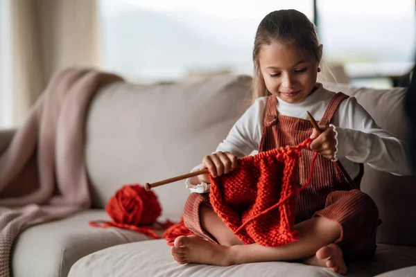 Niña sentada en el sofá y aprendiendo a tejer en casa. — Foto de Stock