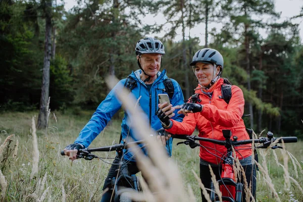 Pareja de ciclistas mayores utilizando teléfono inteligente al aire libre en el bosque en el día de otoño. —  Fotos de Stock