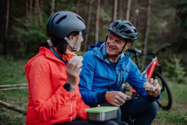 Šťastný starší pár cyklisté s jídlem občerstvení venku v lese na podzim. — Stock fotografie