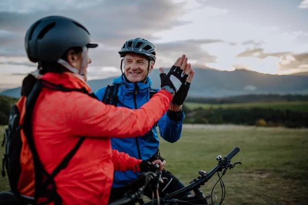 Senior pár bikers high fiving venku v přírodě na podzim den. — Stock fotografie