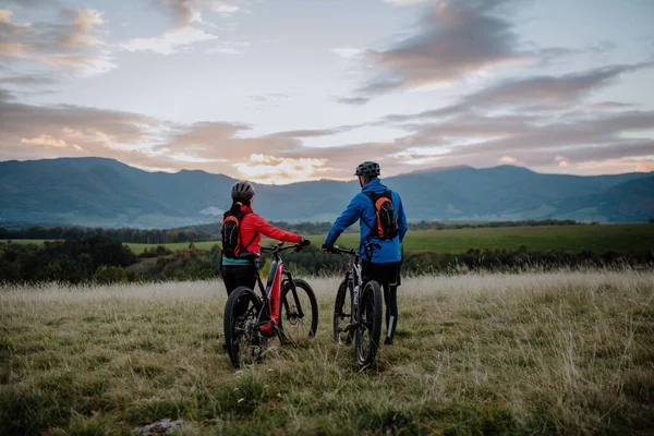 Rückansicht eines Seniorenpaares, das im Herbst im Wald unterwegs ist und E-Bikes schiebt. — Stockfoto