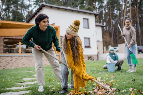 Niñas felices con abuela y madre limpiando el jardín de las hojas en otoño —  Fotos de Stock
