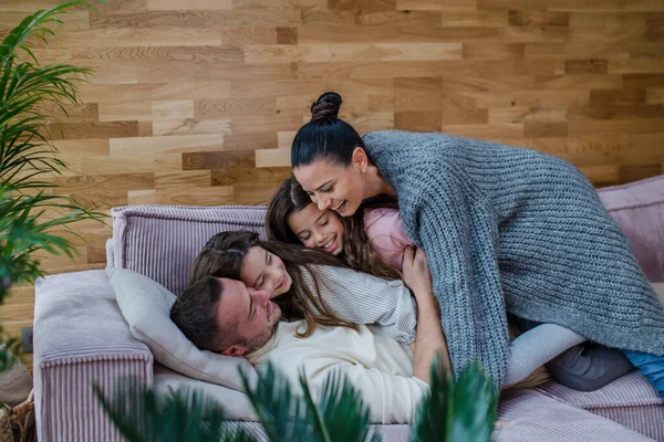Дві щасливі сестри розважаються з батьком над матір'ю, лежачи на дивані вдома . — стокове фото
