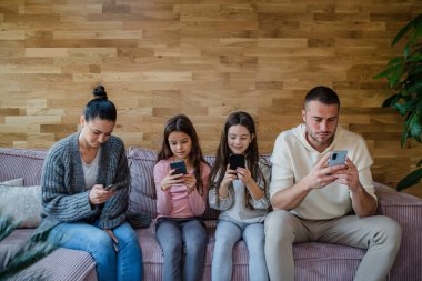 İki küçük kızı olan bir aile, herkes oturma odasında cep telefonu kullanıyor..