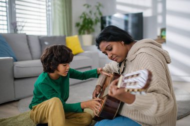 Küçük çok kültürlü çocuk evde annesiyle gitar çalmayı öğreniyor..