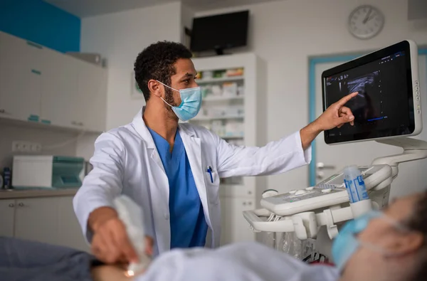 Jonge arts onderzoekt de patiënt met behulp van een echografie apparatuur in de kliniek. — Stockfoto