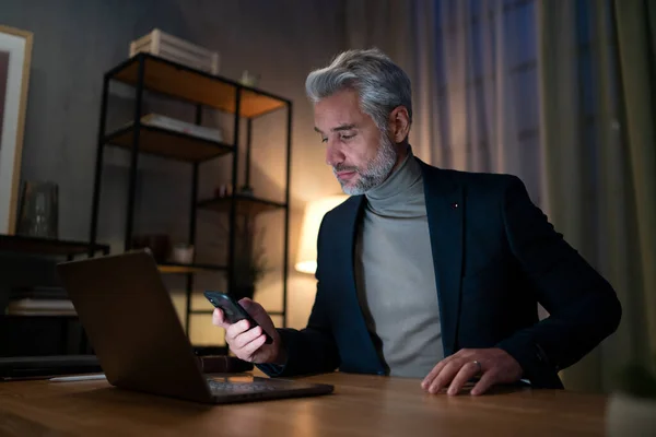 Uomo d'affari maturo che lavora su laptop alla scrivania al chiuso in ufficio di notte. — Foto Stock