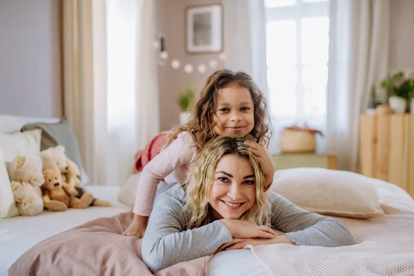 Счастливая маленькая девочка лежит на матерей обратно на кровать и смотрит в камеру дома. — стоковое фото