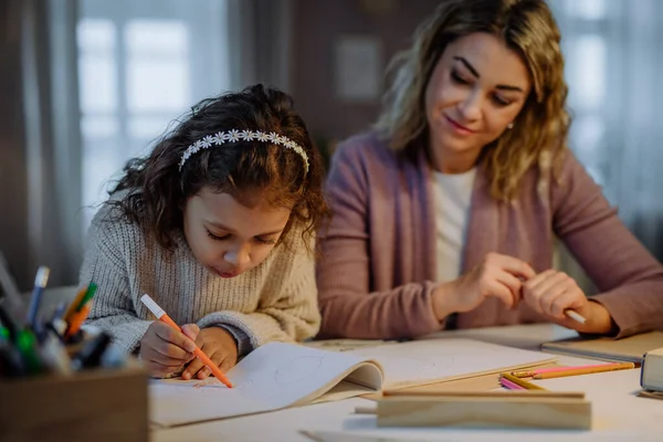 Маленькая девочка делает домашнее задание с матерью вечером дома. — стоковое фото