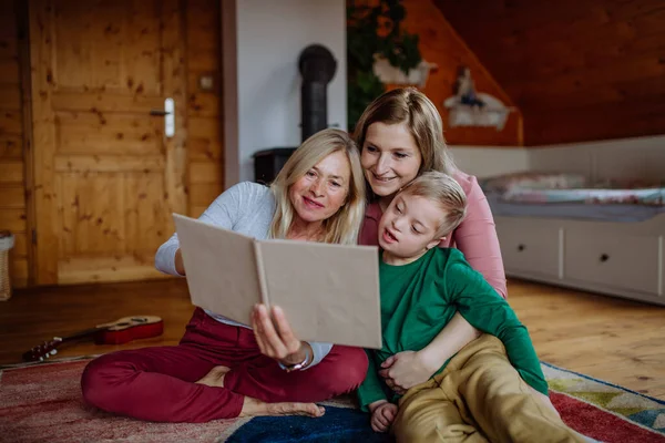 Jongen met Down syndroom met zijn moeder en grootmoeder op zoek naar familie fotoalbum thuis. — Stockfoto