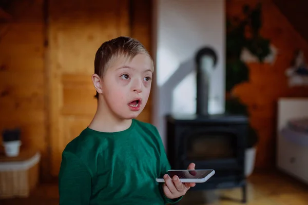 Niño pequeño con síndrome de Down sentado en el suelo y usando el teléfono inteligente en casa. — Foto de Stock