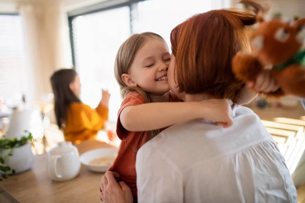 Rear view of mother hugging her little daughter in kitchen at home. — Stock Photo, Image