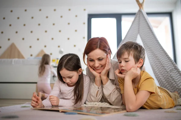 Mutter mit kleinen Kindern liegt auf dem Boden und liest zu Hause Buch. — Stockfoto