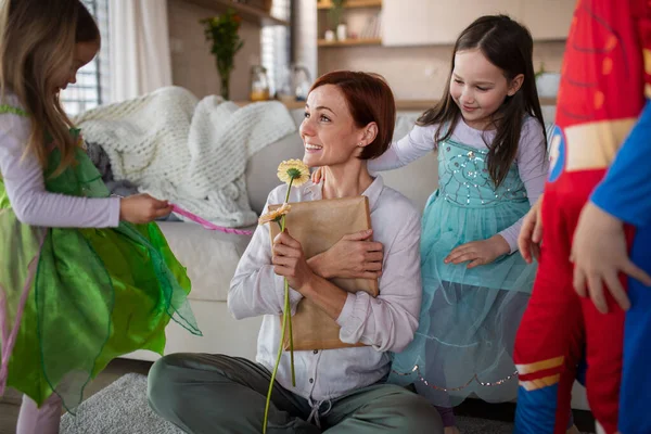 Mother of three little children in costumes getting present and flower from them at home. — Stock Photo, Image