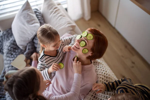 Três crianças colocando pepino no rosto de suas mães em casa. — Fotografia de Stock