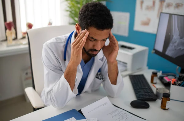Depresso giovane medico maschio con mal di testa seduto nel suo ufficio — Foto Stock