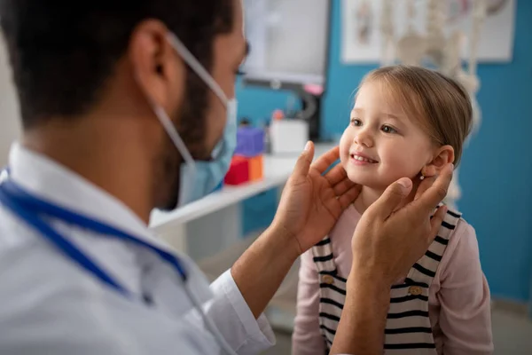 Jonge mannelijke arts controleren van kleine meisjes lymfeklieren in zijn kantoor. — Stockfoto