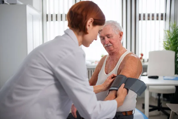 Female doctor measuring blood pressure to senior man patient in her office. — Stock Photo, Image