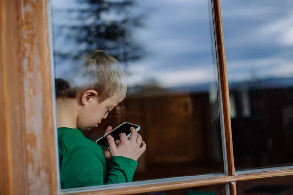 Kleiner Junge mit Down-Syndrom zu Hause mit Smartphone durch Fenster erschossen. — Stockfoto
