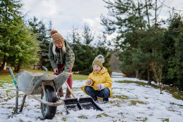 Down sendromlu bir çocuk ve büyükannesi bahçede kar temizliyor.. — Stok fotoğraf