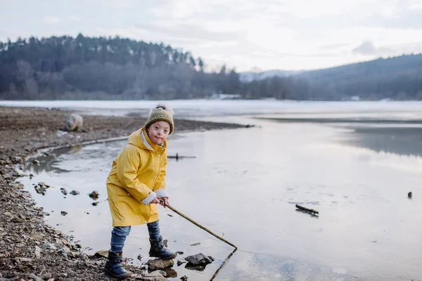 Down sendromlu küçük mutlu çocuk kışın gölün kenarındaki kameraya bakıyor.. — Stok fotoğraf