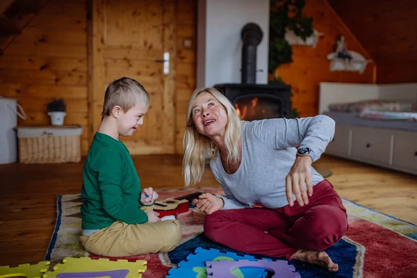 Boy with Down syndroom zitten op de vloer en spelen met zijn grootmoeder thuis — Stockfoto