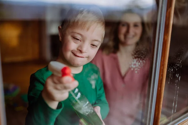 Boy with Down syndrome with his mother cleaning window at home. — Stock Photo, Image