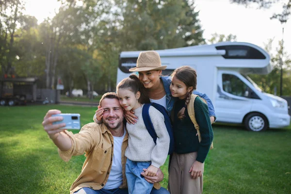 Happy young family with two children ltaking selfie with caravan at background outdoors. — Stock Photo, Image