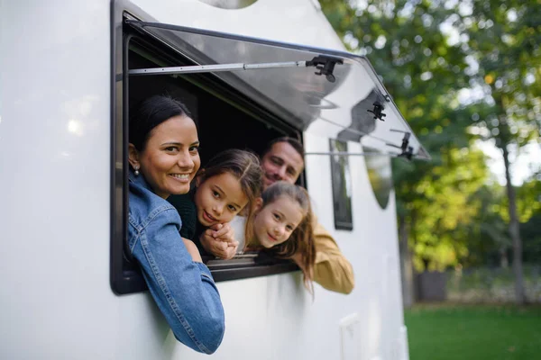 Šťastná mladá rodina se dvěma dětmi hledícími z okna karavany. — Stock fotografie