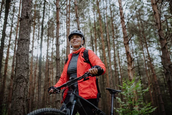 Visão de baixo ângulo da mulher idosa motociclista andando e empurrando bicicleta ao ar livre na floresta no dia de outono. — Fotografia de Stock