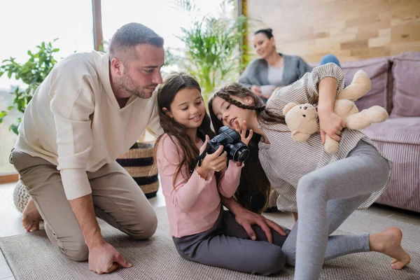Dvě šťastné sestry s otcem sedí na podlaze a učí se používat fotoaparát doma — Stock fotografie