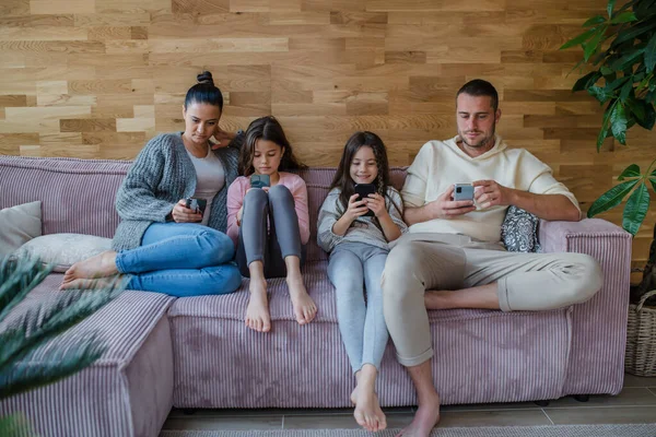 Famiglia con due figlie piccole, tutti usano il cellulare nel soggiorno. — Foto Stock