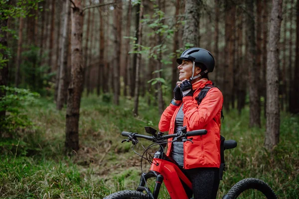 Seniorin setzt bei Herbsttag im Wald Fahrradhelm auf. — Stockfoto