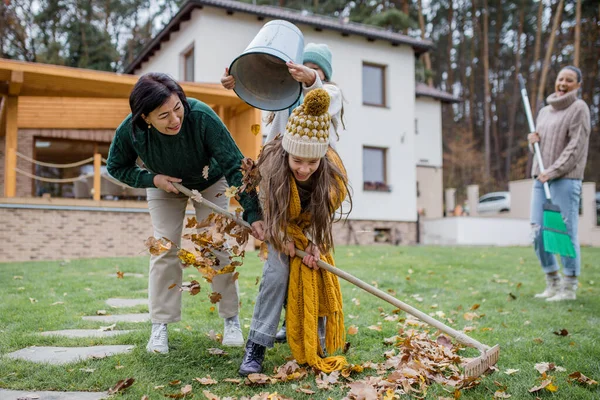 Bambine felici con nonna che raccolgono foglie e le mettono in secchio in giardino in autunno — Foto Stock