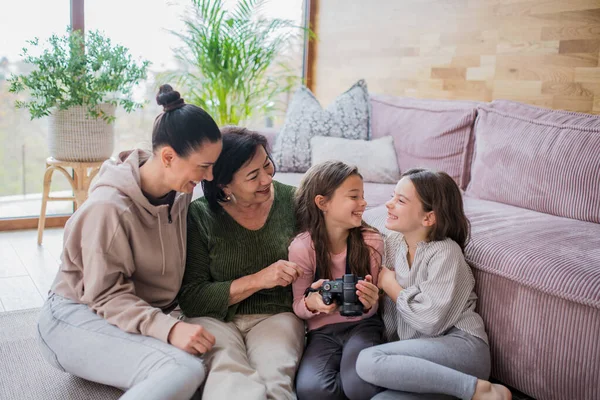 Two happy sisters with mother and grandmother sitting on floor and learning to use camera at home — Φωτογραφία Αρχείου