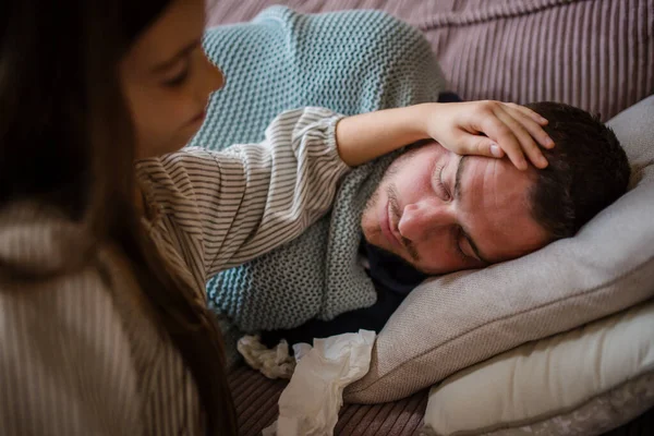 High angle view of little daughter taking care of her sick father at home. — Stock Photo, Image