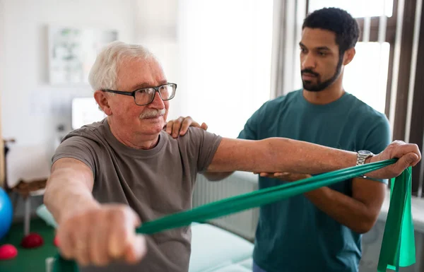 Giovane fisioterapista che si allena con il paziente anziano in una stanza fisica — Foto Stock