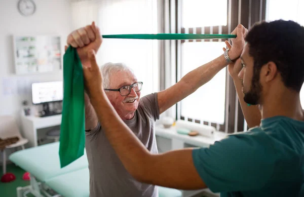 Giovane fisioterapista che si allena con il paziente anziano in una stanza fisica — Foto Stock