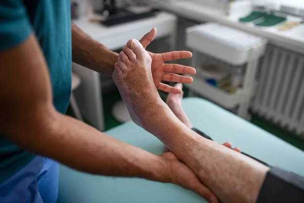 Close-up van de fysiotherapeut die traint met het been van oudere patiënten in een fysiekkamer. — Stockfoto