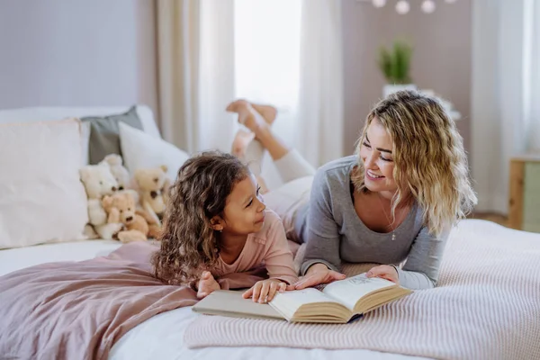 Щаслива мати зі своєю маленькою донькою лежить на ліжку і читає книгу вдома . — стокове фото