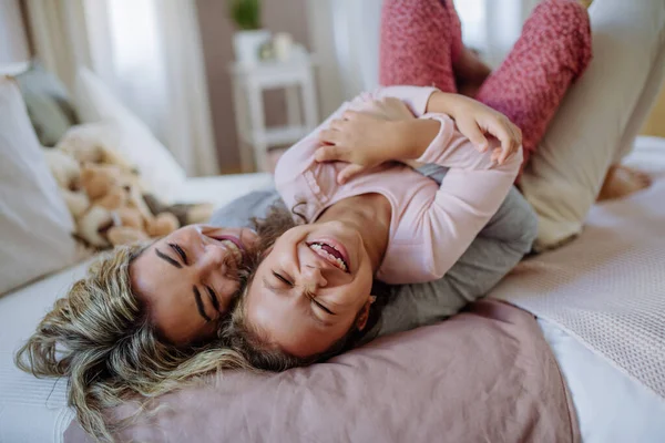 Glückliche Mutter mit ihrer kleinen Tochter, die sich umarmt und zusammen im Bett zu Hause Spaß hat. — Stockfoto