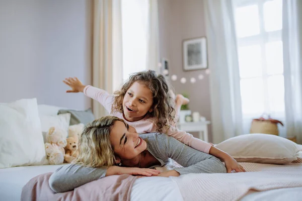 Bonne petite fille couchée sur les mères de retour sur le lit et regardant la caméra à la maison. — Photo