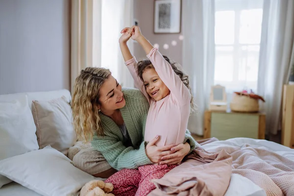 Lycklig mor hamrar sin lilla dotter sträcker sig i sängen när du vaknar på morgonen. — Stockfoto