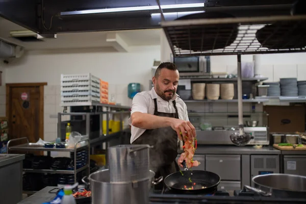 Chef maturo aggiungendo vehetagles tritati in padella al chiuso nella cucina del ristorante. — Foto Stock