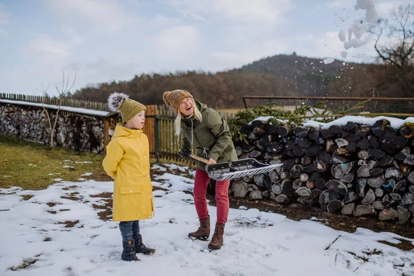 Pojke med Down syndrom med sin mor som rensar snö från vägen med spade framför huset. — Stockfoto