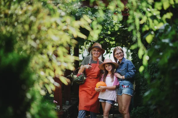 Glückliches kleines Bauernmädchen mit Mutter und Großmutter, die im Garten in die Kamera schauen — Stockfoto